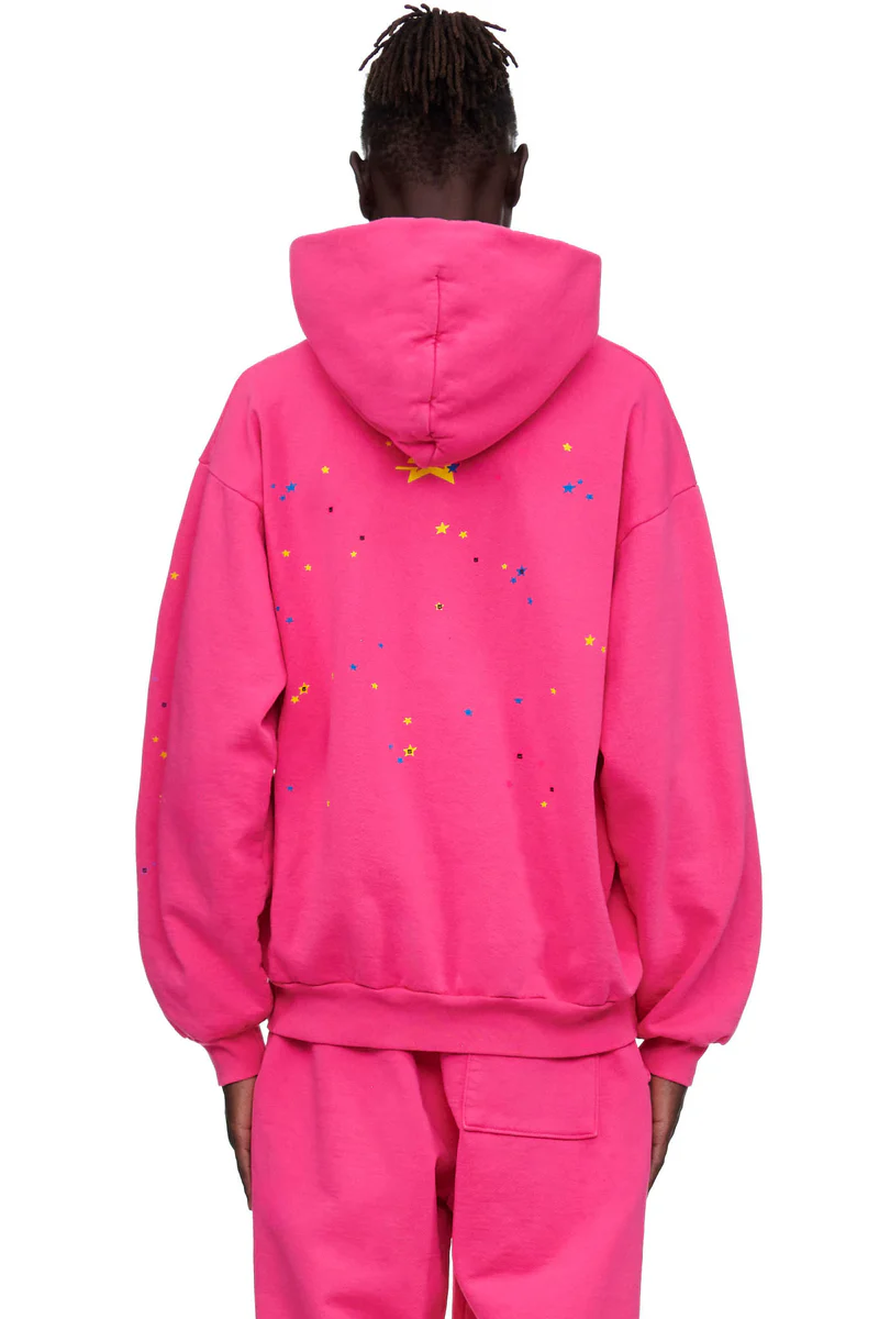 Back view of a man in a magenta Sp5der P*NK hoodie and matching sweatpants, the hood lying flat between the shoulders with small yellow and blue stars and tiny dark dots printed across the back