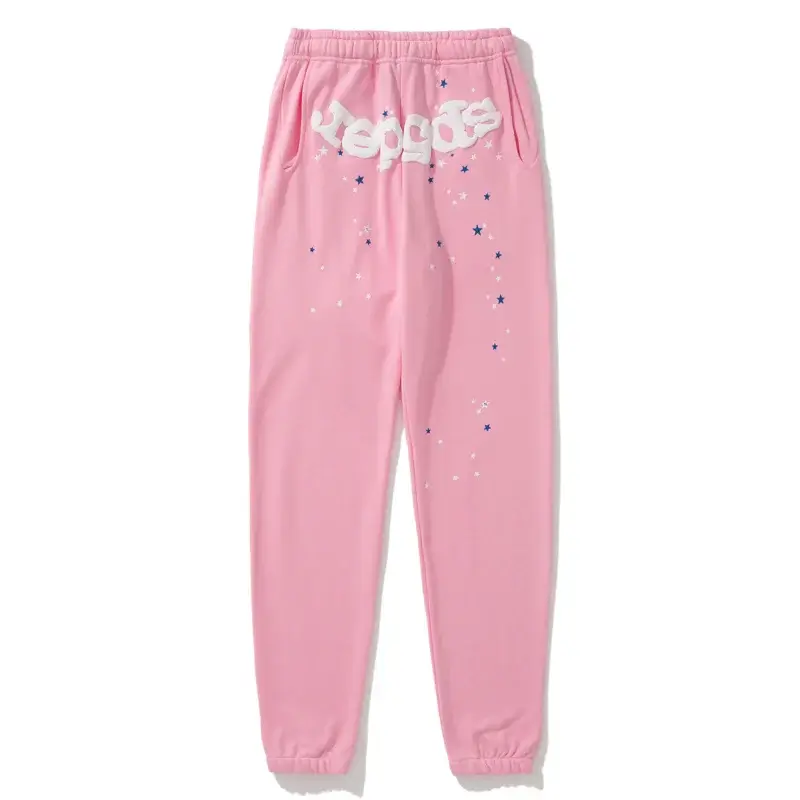 Pale bubblegum pink Sp5der sweatpants laid flat with a white puff sp5der wordmark near the waistband and scattered navy and white stars running down one leg to a cuffed ankle